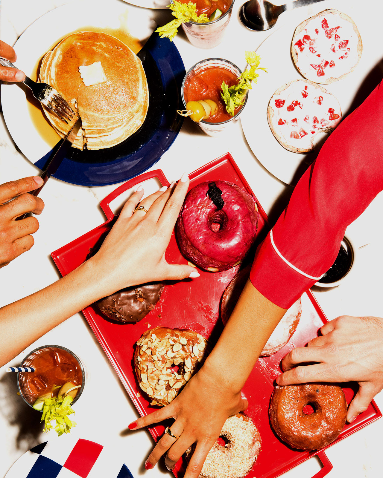 An overshot image of hands reaching for tasty bites like donuts, pancakes and bloody marys.
